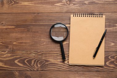 Blank notebook, magnifier and pen on wooden background. World Poetry Day celebration