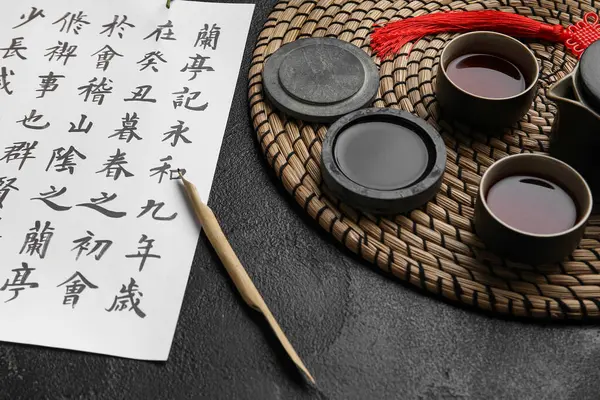 Asya hiyeroglifleri, mürekkep, uçlu kalem ve koyu arka planda bir fincan çay, yakın plan. Uluslararası Haiku Şiir Günü