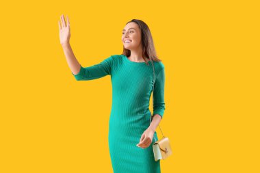 Sarı arka planda el sallayan güzel genç bir kadın.