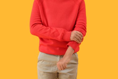 Küçük çocuk sarı arka planda kolunu kıvırıyor.