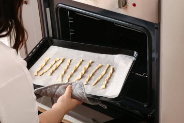 Bir kadın çiğ İtalyan Grissini ile pişirme tepsisini fırına koyuyor.