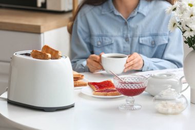 Kadın, modern tost makinesi ve lezzetli reçelli tostlarla kahvaltı yapıyor.