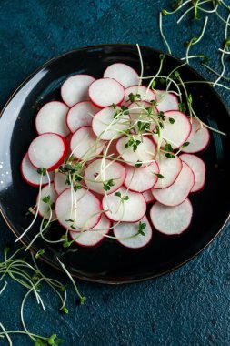 Dilimlenmiş taze turp ve mavi grunge arka planda mikroyeşillikler.