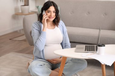 Evde çalışan hamile bir kadın cep telefonuyla konuşuyor.