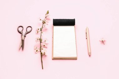 Pembe arka planda çiçek açan ağaç dalı, defter, kalem ve makas bileşimi
