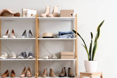 Değişik kadın ayakkabılarına, kıyafetlerine ve çiçeklerine sahip raf ünitesi butikte ışık duvarının yanında.