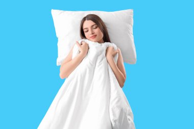 Mavi arka planda yumuşak yastıklı ve battaniyeli genç kadın.