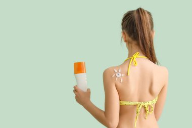 Soluk yeşil arka planda güneş kremi şişesi olan küçük kız.