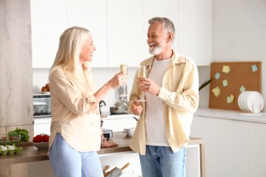 Olgun bir çift mutfakta şampanya içiyor.