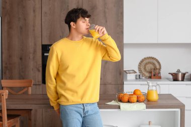 Genç adam mutfakta portakal suyu içiyor.