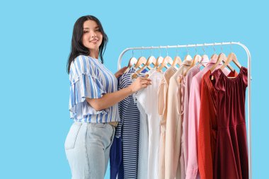 Güzel genç bir kadın mavi arka planda kıyafet seçiyor.