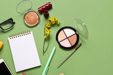 Makyaj malzemesi, gözlük, güzel çiçekler ve yeşil arka planda not defteri olan kompozisyon