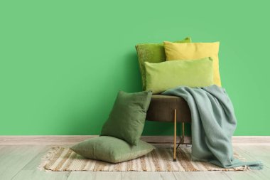 Ottoman with soft cushions near green wall