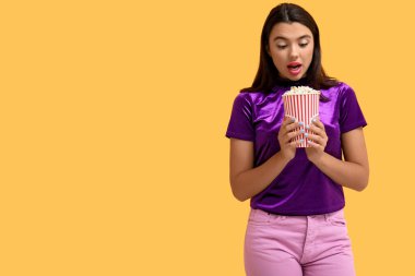 Sarı arka planda bir kova patlamış mısırla güzel, şaşırmış bir kadın.