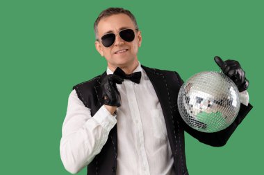 Yeşil arka planda disko topu olan takım elbiseli havalı olgun bir adam.