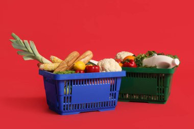 Kırmızı arka planda yiyecek dolu alışveriş sepetleri.