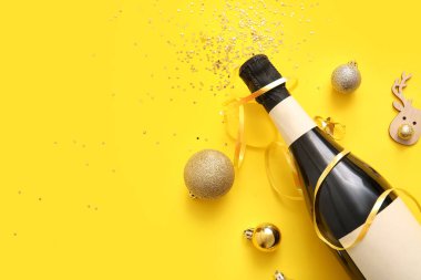 Sarı arka planda Noel süslemeleri olan bir şişe şampanya.