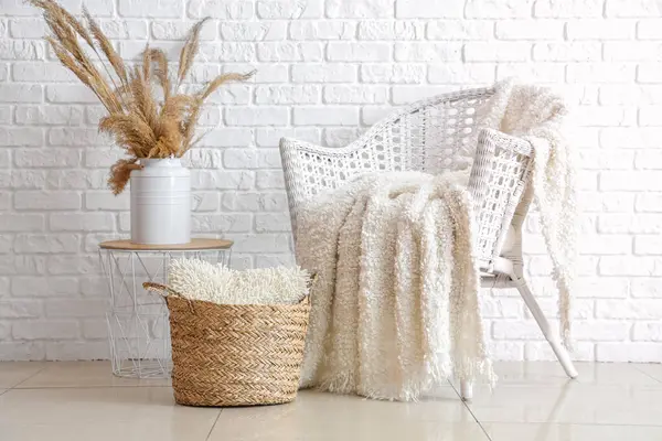 Ekose örülmüş Rattan koltuğu ve beyaz tuğla duvarın yanında yastıklı hasır sepet.