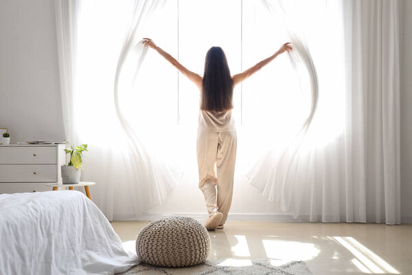 Утро красивой молодой женщины, открывающей шторы в спальне