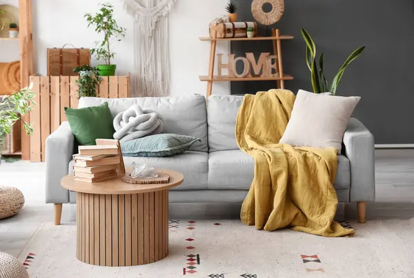 Aydınlık oturma odasının içinde şık gri kanepe ve ahşap sehpa var.