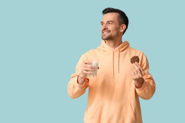 Lezzetli kurabiyesi ve mavi arka planda bir bardak sütü olan yakışıklı adam.