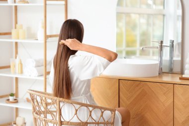 Genç esmer kadın banyoda saçlarını tarıyor.