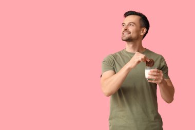 Tatlı kurabiyesi ve pembe arka planda bir bardak sütü olan yakışıklı bir adam.