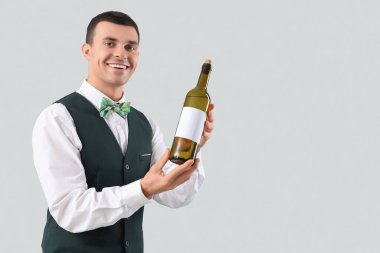 Gri arka planda şarap şişesi olan genç bir barmen.