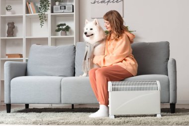 Samoyed köpekli genç kadın evdeki radyatörün yanındaki kanepede.