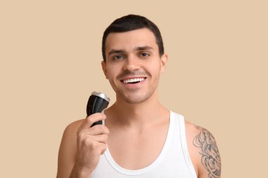 Bej arka planda elektrikli tıraş makinesi olan yakışıklı bir genç.