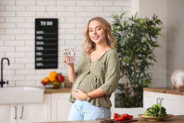 Mutfakta bir bardak suyu olan hamile bir kadın.