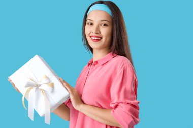 Mavi arka planda hediye kutusu olan güzel bir Asyalı kadın.