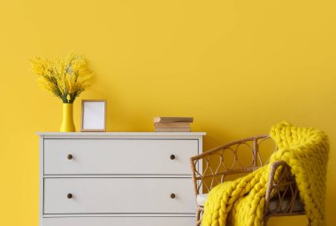 Sarı duvarın yanında koltuk ve örgü battaniyeli dolap.