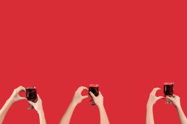 Kırmızı arka planda sıcak şarap kadehleriyle kadın elleri.