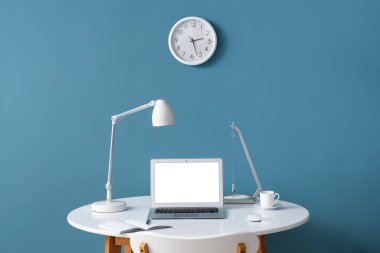 Modern dizüstü bilgisayarı, not defteri ve renkli duvarın yanında bir fincan kahvesi olan şık bir iş yeri.