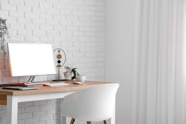 Modern bilgisayarlı, ışıklı tuğla duvarın yanında şık bir iş yeri.