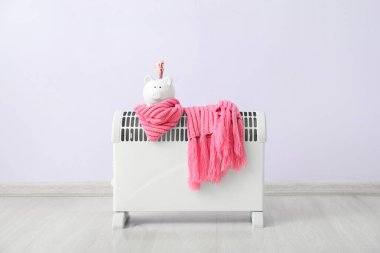 Kumbarası, parası ve atkısı olan elektrikli ısıtıcı, leylak duvarın yanında. Isınma mevsimi kavramı