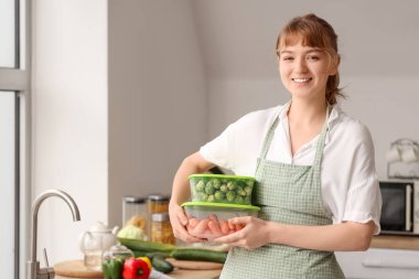 Mutfakta dondurulmuş sebzelerle plastik kaplar tutan güzel genç bir kadın.