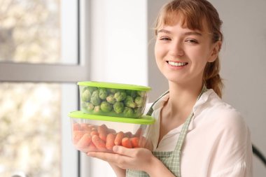 Mutfakta dondurulmuş sebzelerle plastik kaplar tutan güzel genç bir kadın.