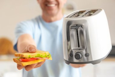 Modern ekmek kızartma makinesi ve lezzetli sandviçiyle orta yaşlı bir adam, yakın plan.