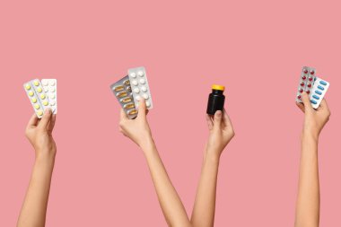 Kadın eli su toplayan hapları tutuyor ve pembe arka planda ilaç şişesi var.