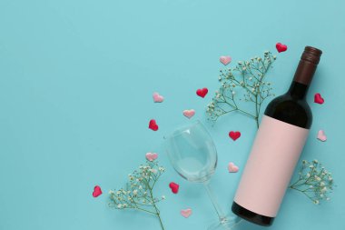 Bottle of wine, glass and flowers on turquoise background. Valentine's Day celebration
