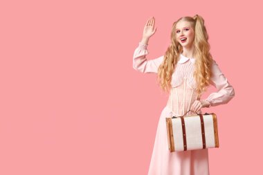 Güzel, genç ve mutlu bir kadın. Bebek gibi giyinmiş. Pembe arka planda el sallıyor.