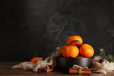 Bowl with tasty tangerines and cinnamon on wooden table