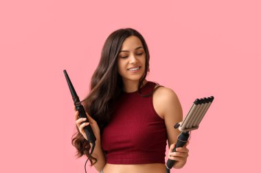 Beautiful young woman with different curling irons on pink background