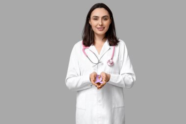 Gri arka planda açık mor kurdeleli genç bayan doktor. Testis kanseri farkındalığı