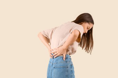 Bej arka planda sırt ağrısı çeken genç bir kadın.