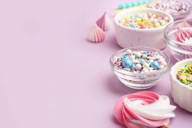 Rengarenk tatlı serpiştirilmiş kaseler ve leylak arkaplanda krema