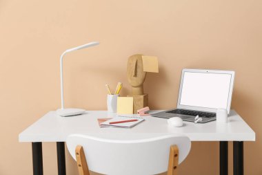 Ofisteki masada dizüstü bilgisayar, kablosuz kulaklık, lamba ve defter.