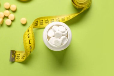 Kilo verme haplarıyla dolu bir şişe ve yeşil arka planda şerit.